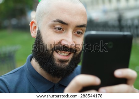 Bearded bald man sitting on a bench and game on tablet at the alley
