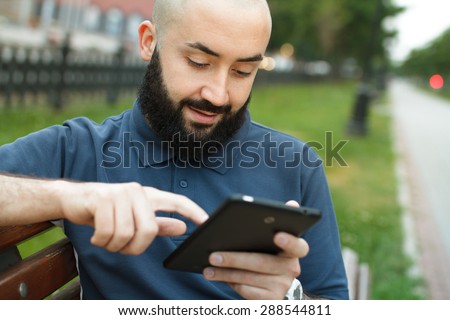 Bearded bald man sitting on a bench and read tablet at the alley