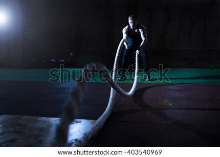 Athletic man doing some cross-training exercises with a rope in gym
