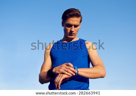 Young handsome athletic man checking his pulse on sport watch