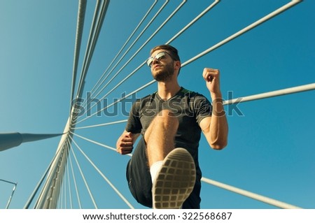 Low angle view of a handsome urban jogger running over the bridge
