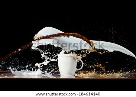 Coffee and milk pouring in a cup with splashes and drops, on black background