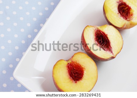 White platter/plate on pale baby blue polka dot table cloth with 3 sliced peaches. Focus on one peach