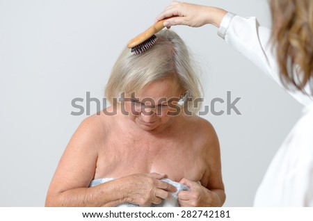 Elderly lady gets her hair combed, maybe she lives in a home for old people and needs care