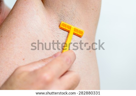 Man shaving the hairs under his armpit with a handheld razor, close up of his underarm and hand