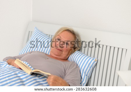 Middle Aged Woman Holding a Novel Book While Lying on her Bed and Looking at the Camera.