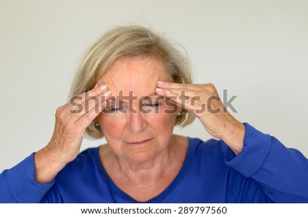 Senior lady suffering with a headache or fever holding her hand to her forehead with her eyes closed in pain, head and shoulders over gray