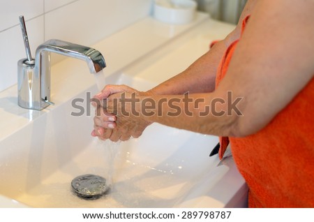 Woman washing her hands at the sink rinsing off the soap under the running water from the faucet