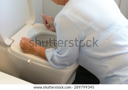 Woman getting sick and vomiting over a toilet bowl kneeling down with her arms resting on the seat, close up view of her body