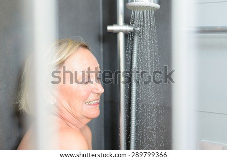Smiling attractive senior woman taking a shower looking through the open door of the shower cubicle and smiling at the camera
