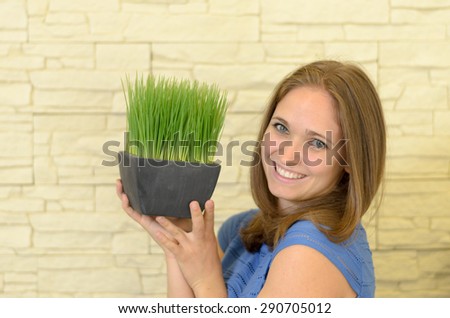 Close up Happy Young Woman Holding a Small Green Plant in a Vase Up High While Looking at the Camera.