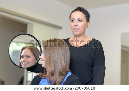 Satisfied Girl Customer Looking at Herself on the Mirror Hold by a Hairstylist After Fixing her Hair Inside the Salon.