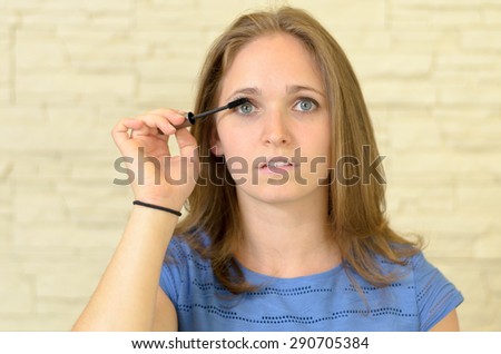Pretty young woman applying eyeliner to her eye to enhance and outline the eye in a fashion and beauty concept