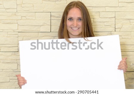 Pretty woman holding up a blank white sign in front of her chest as she gives the camera a lovely smile - copyspace for your text or advertising