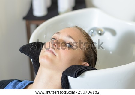 Young woman in a hairdressing salon lying back with her head in the basin waiting for her hair to be shampooed before cutting it