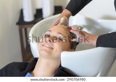 Woman having her hair shampooed in a professional hair salon smiling as the hairdresser massages her head