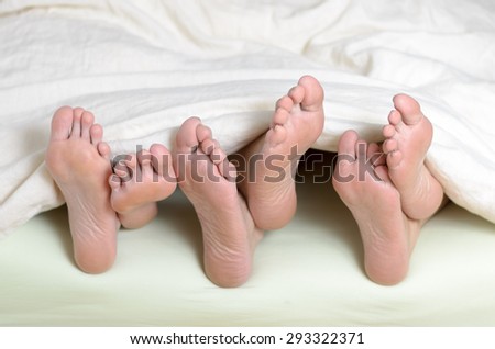 Three pairs of feet in bed, one above the other
