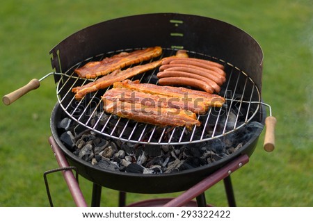 Spicy sausages over a portable barbecue outdoors on green grass at a summer picnic or campsite