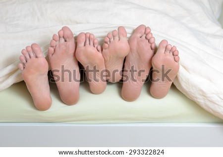 Three pairs of feet in bed, mixed up