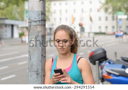 Young woman in a trendy summer top texting on her mobile phone as she walks down and urban street past a streetlamp pole