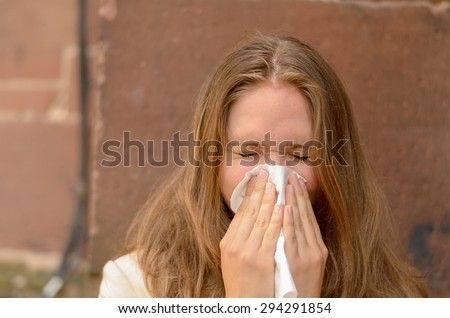Young woman blowing her nose on a handkerchief conceptual of an illness, flu, cold, allergic rhinitis or hay fever