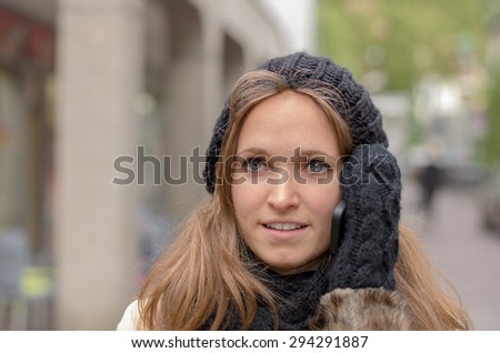 Young woman chatting on her mobile in winter holding the phone to her ear with a gloved hand as she smiles while listening to the conversation, closeup headshot outdoors in town