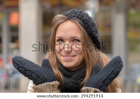 Attractive charismatic young woman in winter fashion making a gesture with her gloved hands as she gives the camera a beaming smile