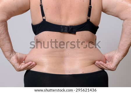 Senior woman squeezing her excess fat over her hips at the back between her fingers as she poses in her panties and bra, close up torso view