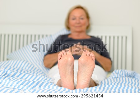 View of the soles and bare feet of a woman relaxing on her bed with selective focus to the soles and a toe to head perspective