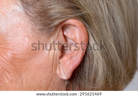 Close up of the ear of an elderly woman with her blond ear tucked back behind the ear to expose the lobe