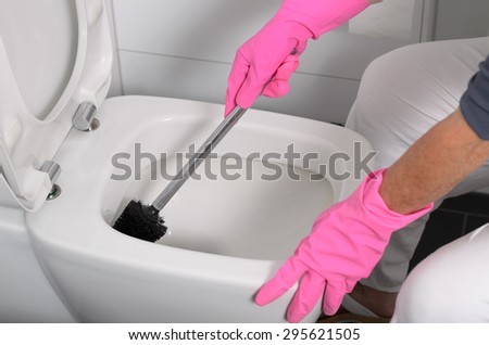 Woman in pink gloves cleaning out the toilet bowl with a brush to remove germs and bacteria under the rim in a concept of cleanliness, hygiene and household chores