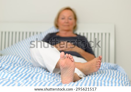 View of the sole and bare foot of a woman relaxing on her bed with selective focus to the sole and a toe to head perspective