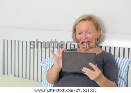 Elderly woman using a tablet computer as she relaxes on her bed surfing the internet and social media