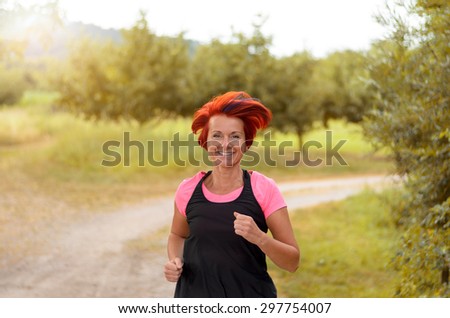 Half Body Shot of a Healthy Middle Aged Woman Jogging Along the Outdoor Pathway and Looking at the Camera with Happy Facial Expression.