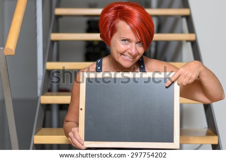 Close up Adult Redhead Woman Holding Small Chalkboard with Copy Space While Sitting on the Stairs and Smiling at the Camera.