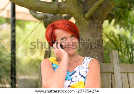 Close up Thoughtful Adult Woman Talking to Someone on her Mobile Phone While Sitting on the Bench Under the Tree.