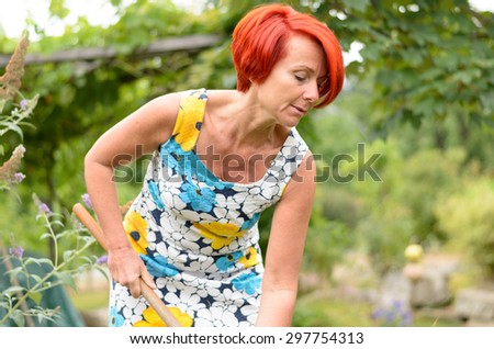 Adult Redhead Woman in a Floral Dress, Raking the Flower Garden at the Backyard Alone.