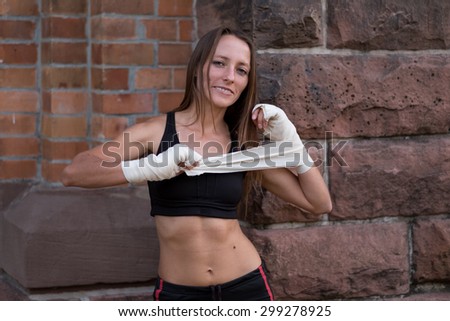 Friendly smiling female boxer wrapping her hands in bandages before starting a training session at the gym or entering a fight