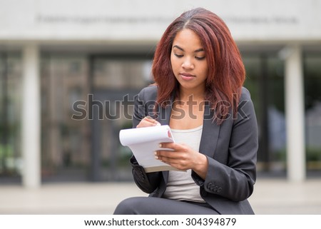 Half Body Shot of a Young Female Business Student Writing Some Notes at the Bench Outside the School Building