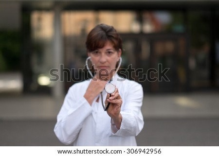 Half Body Shot of a Young Female Medical Doctor with Stethoscope Standing Outside the Hospital and Looking at the Camera.