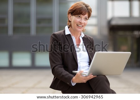 Businesswoman sitting thinking with her laptop balanced on her lap as she contemplates information she has just read on the screen as she relaxes outside the office