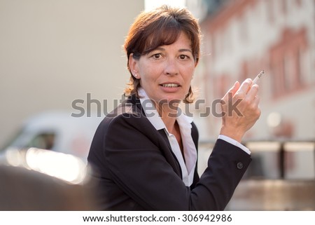 Attractive businesswoman taking a smoke break at the office standing outdoors looking at the camera with a guilty expression and a cigarette in her hand