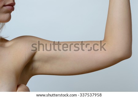 Young blond woman showing flabby arm, effect of aging caused by loss of elasticity and muscle, close-up