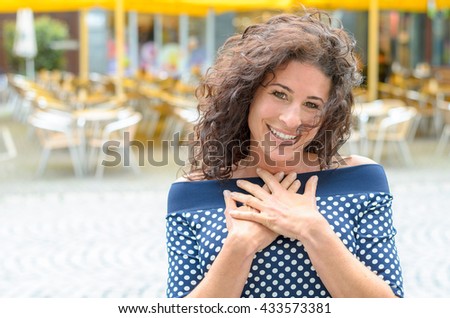 Grateful young woman with her hands to her heart standing outdoors in an town square smiling at the camera in gratitude