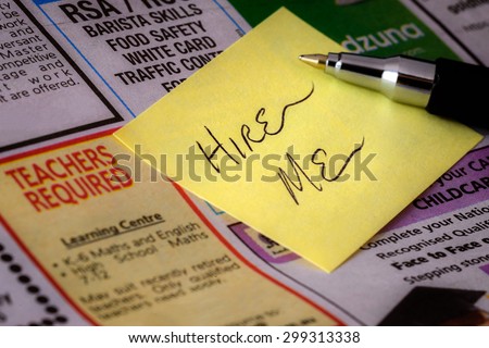 Handwritten stylized \'Hire Me\' sticker note on jobs advertising section of newspaper.