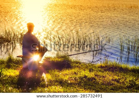 Evening fishing on the lake. The fisherman\'s silhouette on a sunset