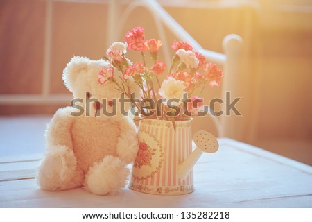 Still life with teddy bear and pink flowers in the watering can with back light