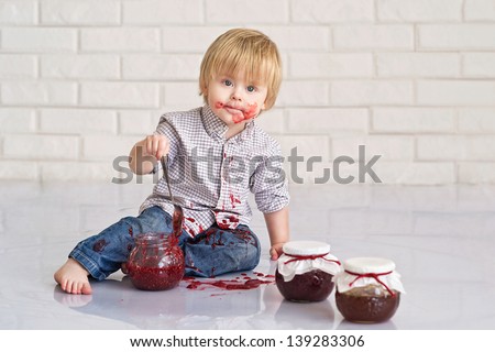 Funny little boy got messy eating strawberry jam from glass jars