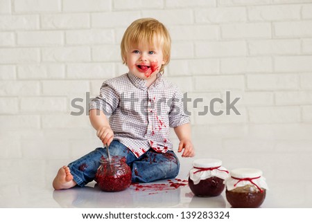 Adorable little boy got messy eating strawberry jam from glass jars