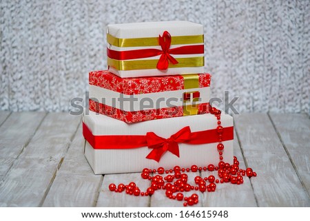 Stack of wrapped gift boxes with ribbons and red beads as Christmas presents on the wooden floor